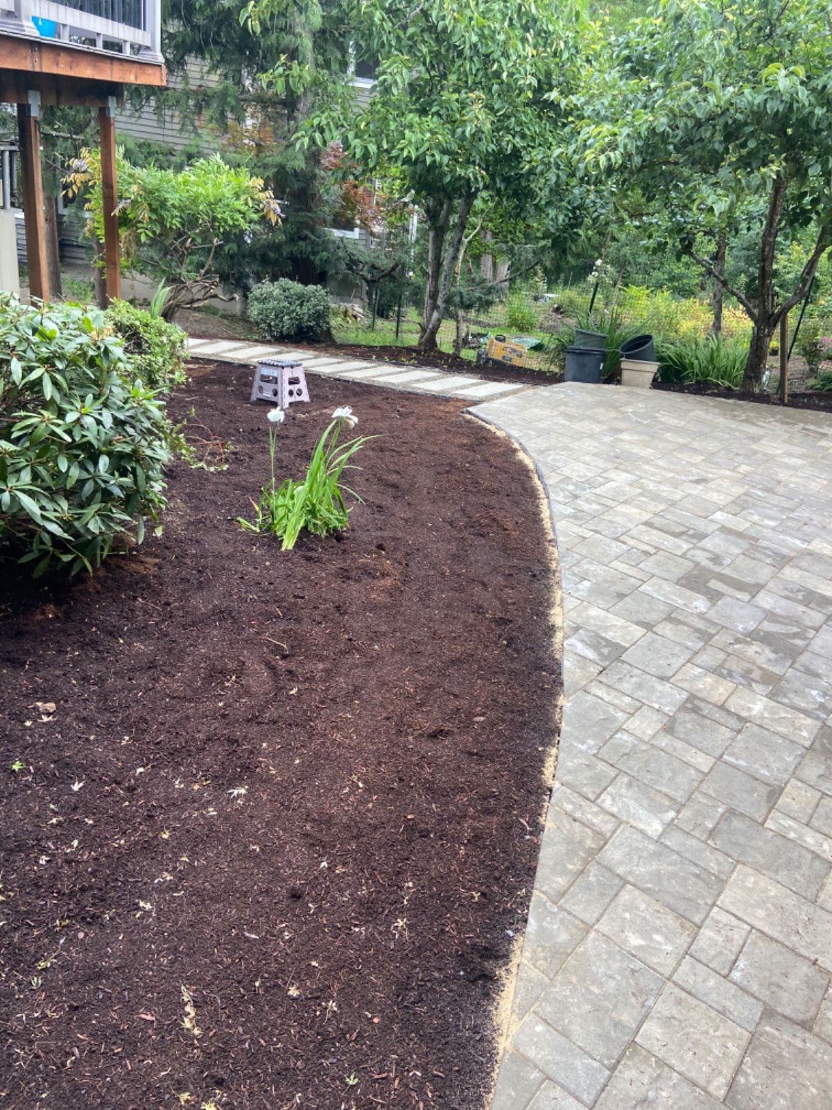 A brick walkway leading to a lush green garden surrounded by trees and bushes.