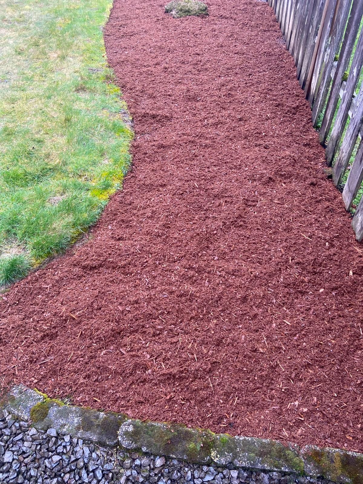 A path lined with red mulch next to a fence.