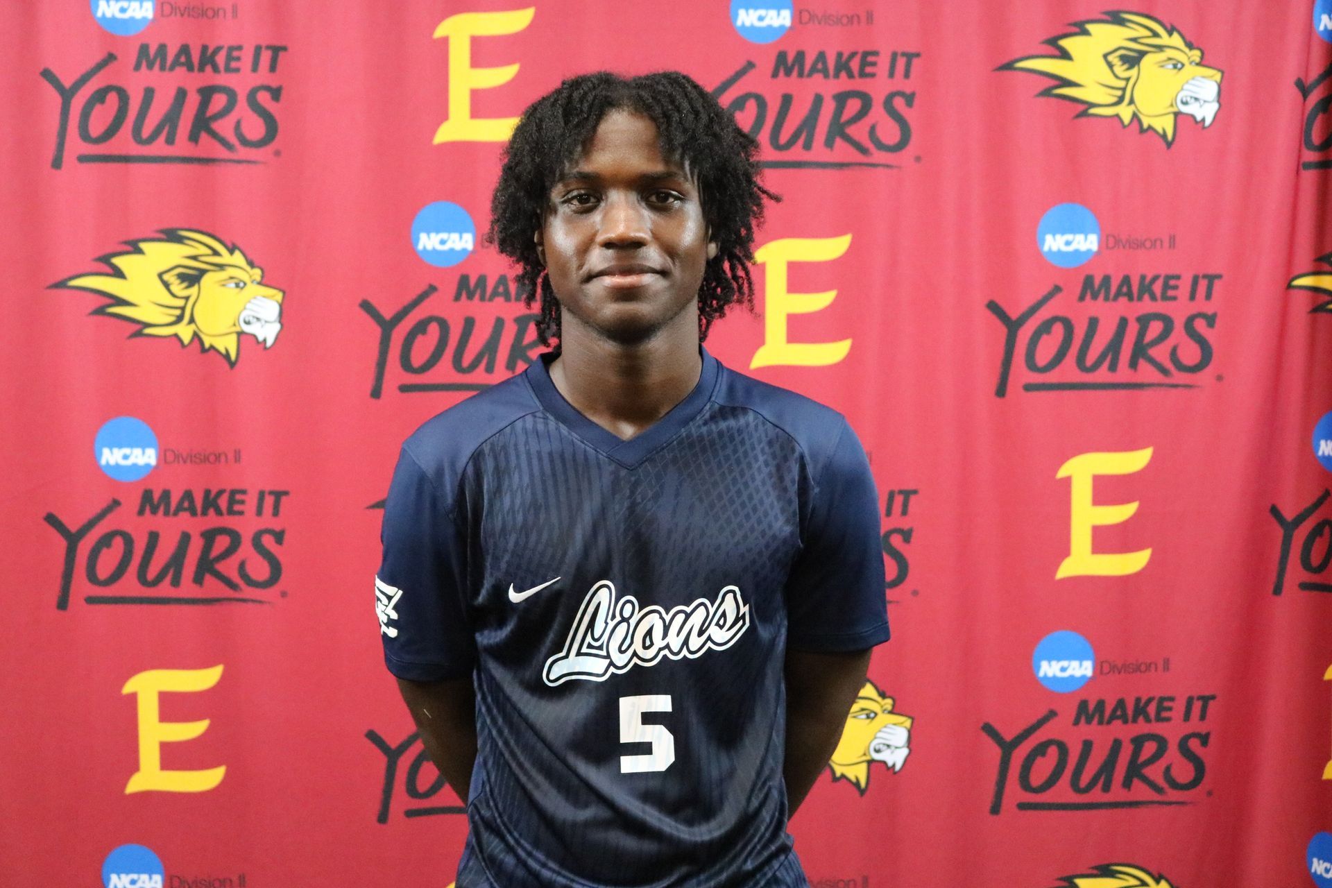 A man wearing a number 5 jersey stands in front of a make it yours banner