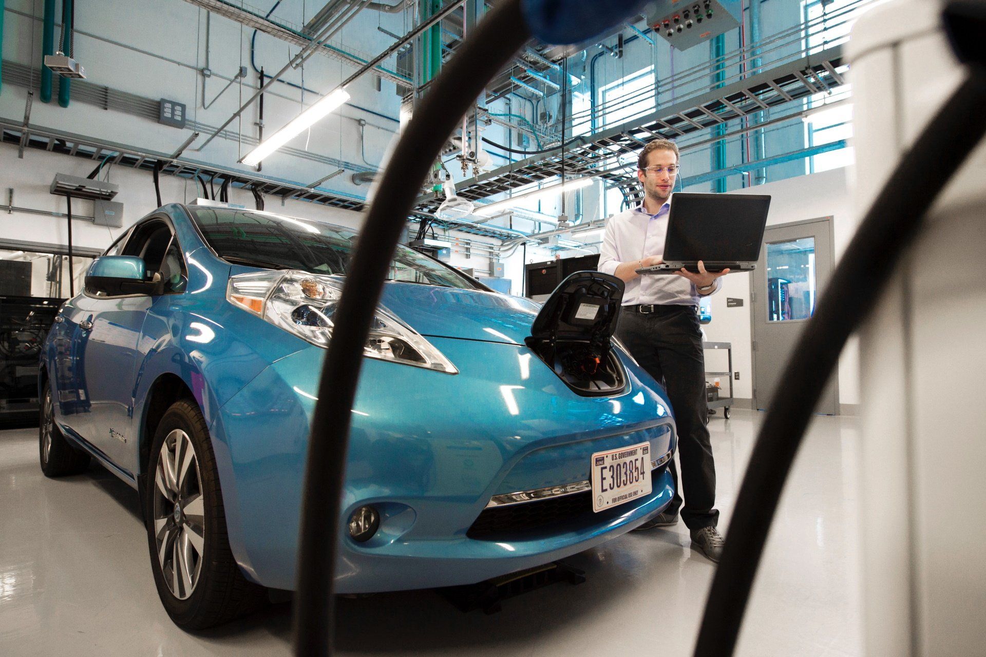 A man is standing next to a blue electric car in a garage.