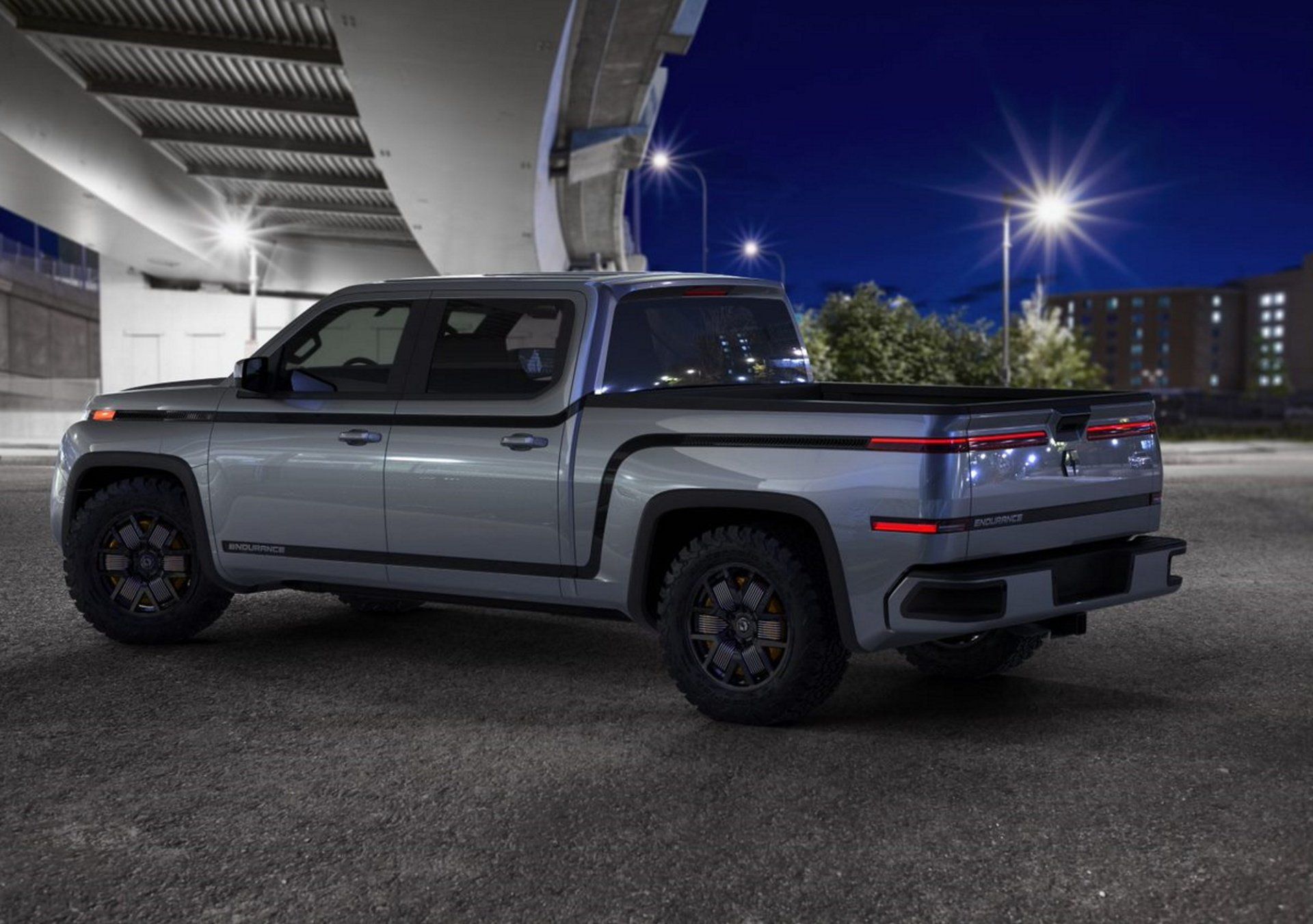 A silver truck is parked under a bridge at night.