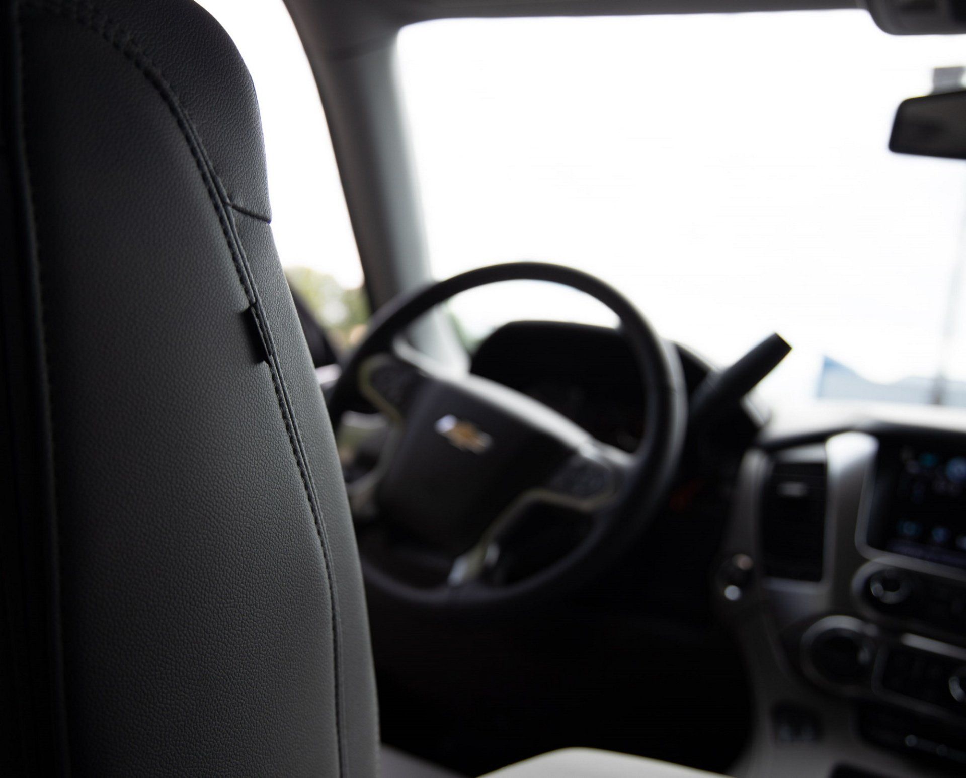 A close up of a car seat with a steering wheel in the background