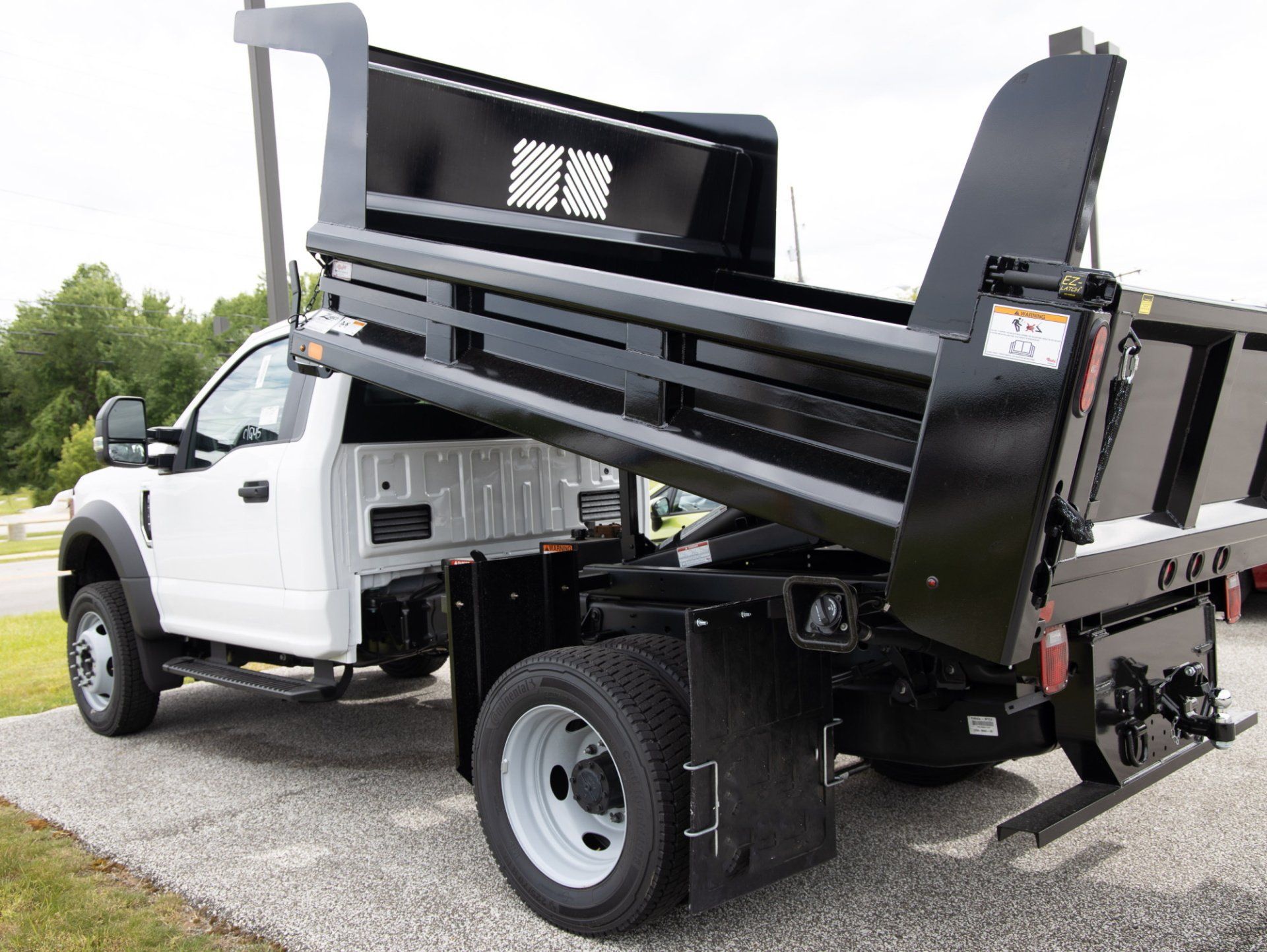 A white dump truck with a black dump bed is parked on the side of the road.
