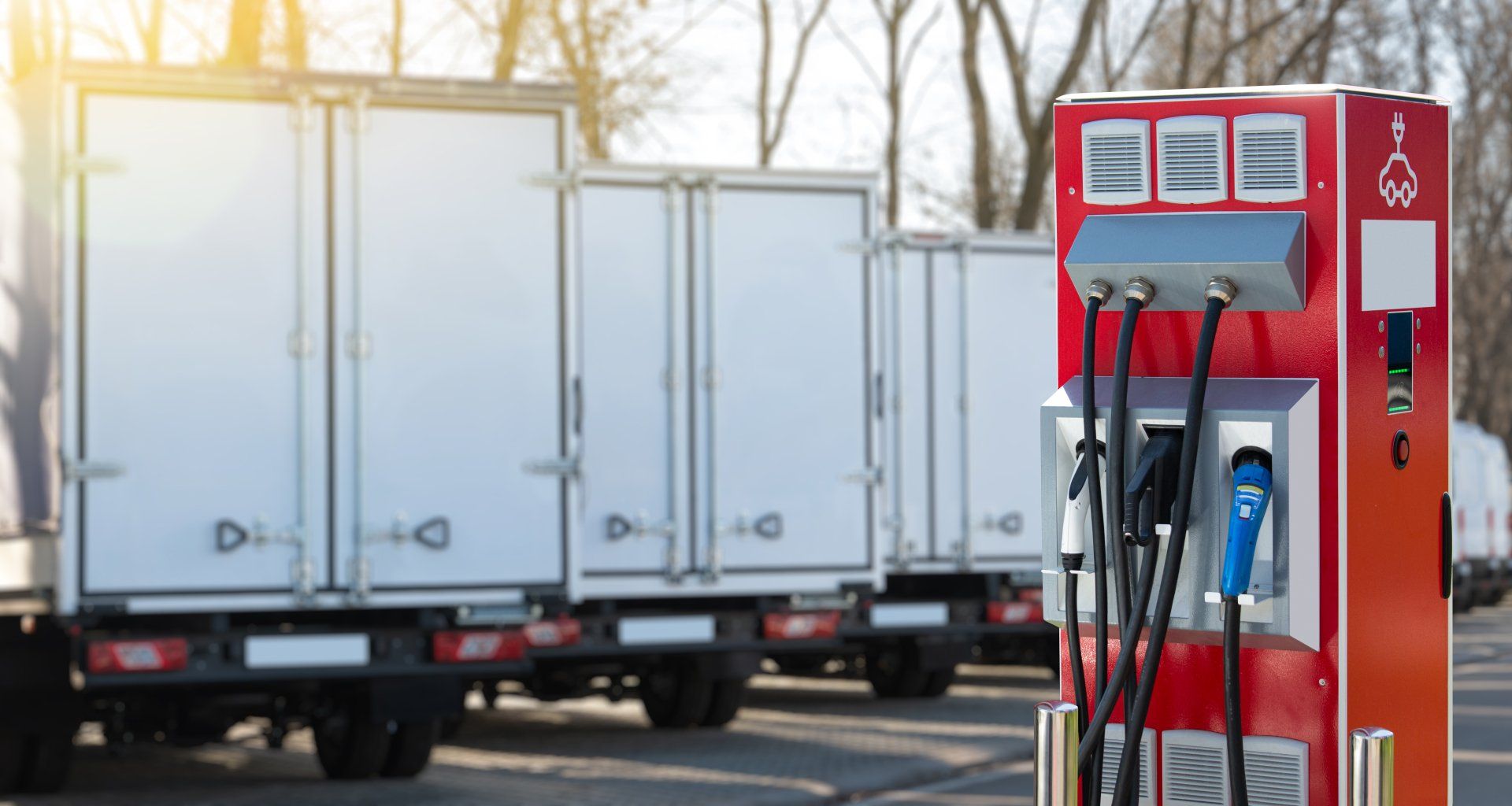 A row of white trucks are parked next to a red charging station.