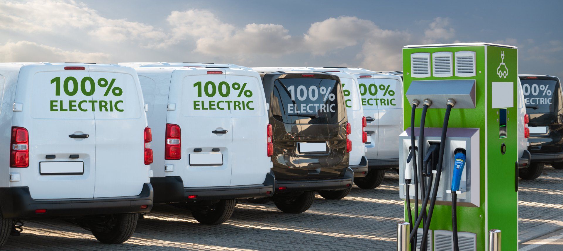 A row of electric vans are parked next to each other at a charging station.