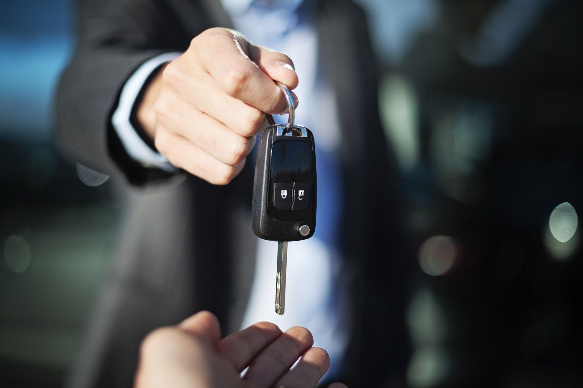A man in a suit is handing a car key to another person