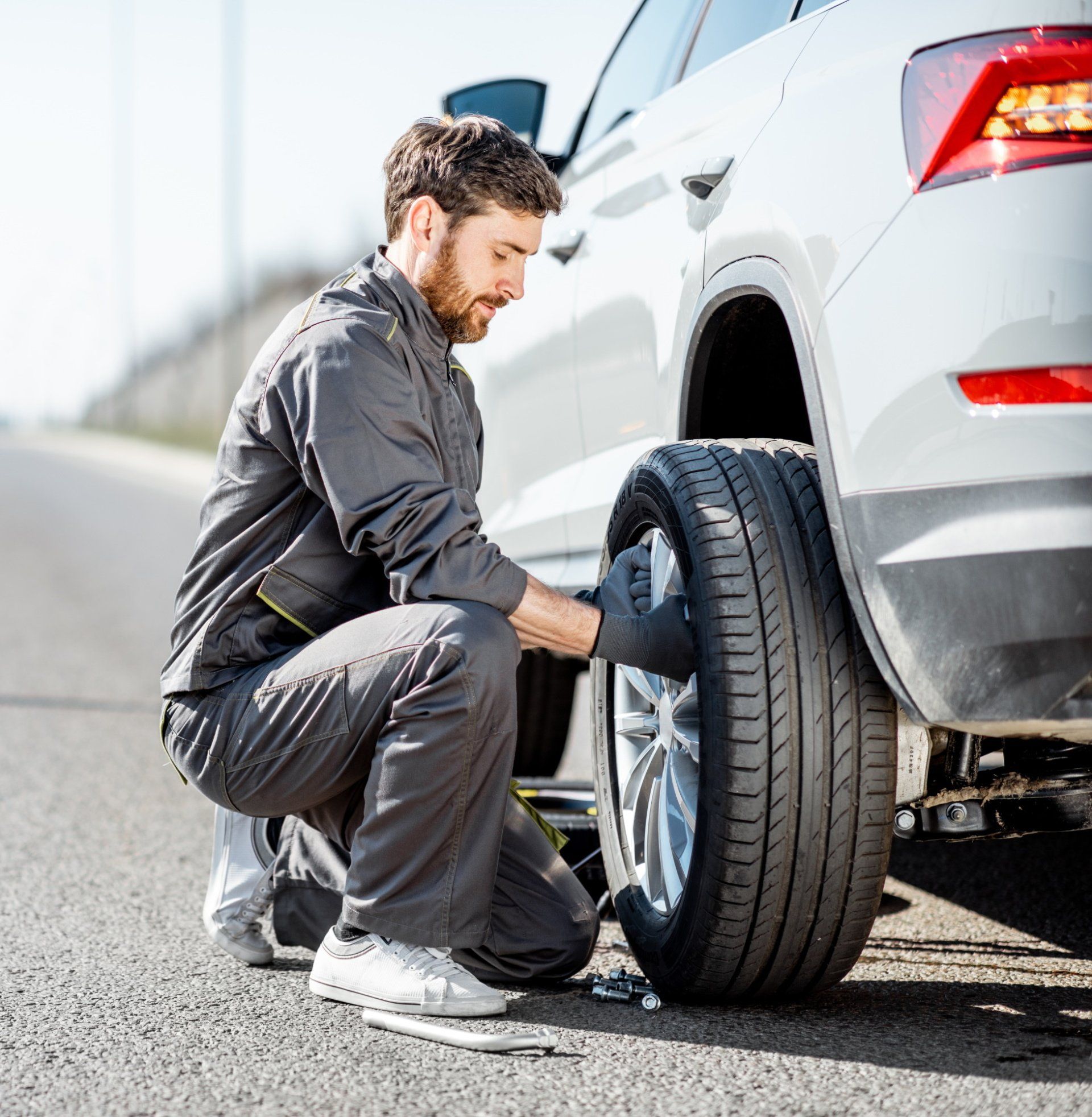 A man is changing a tire on a car on the side of the road.