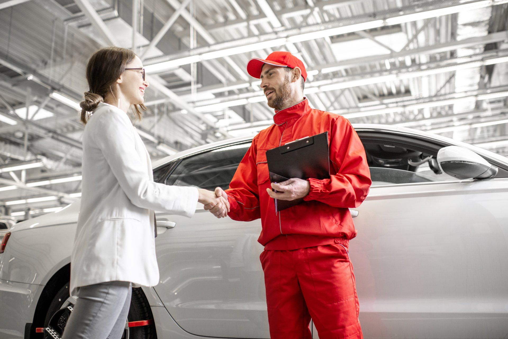 A woman is shaking hands with a mechanic in a garage.