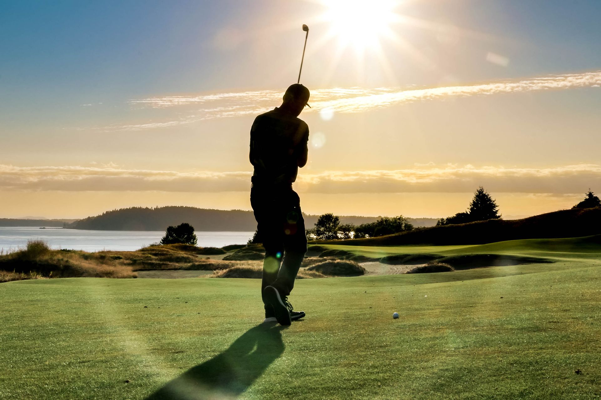 A man is swinging a golf club on a golf course at sunset.