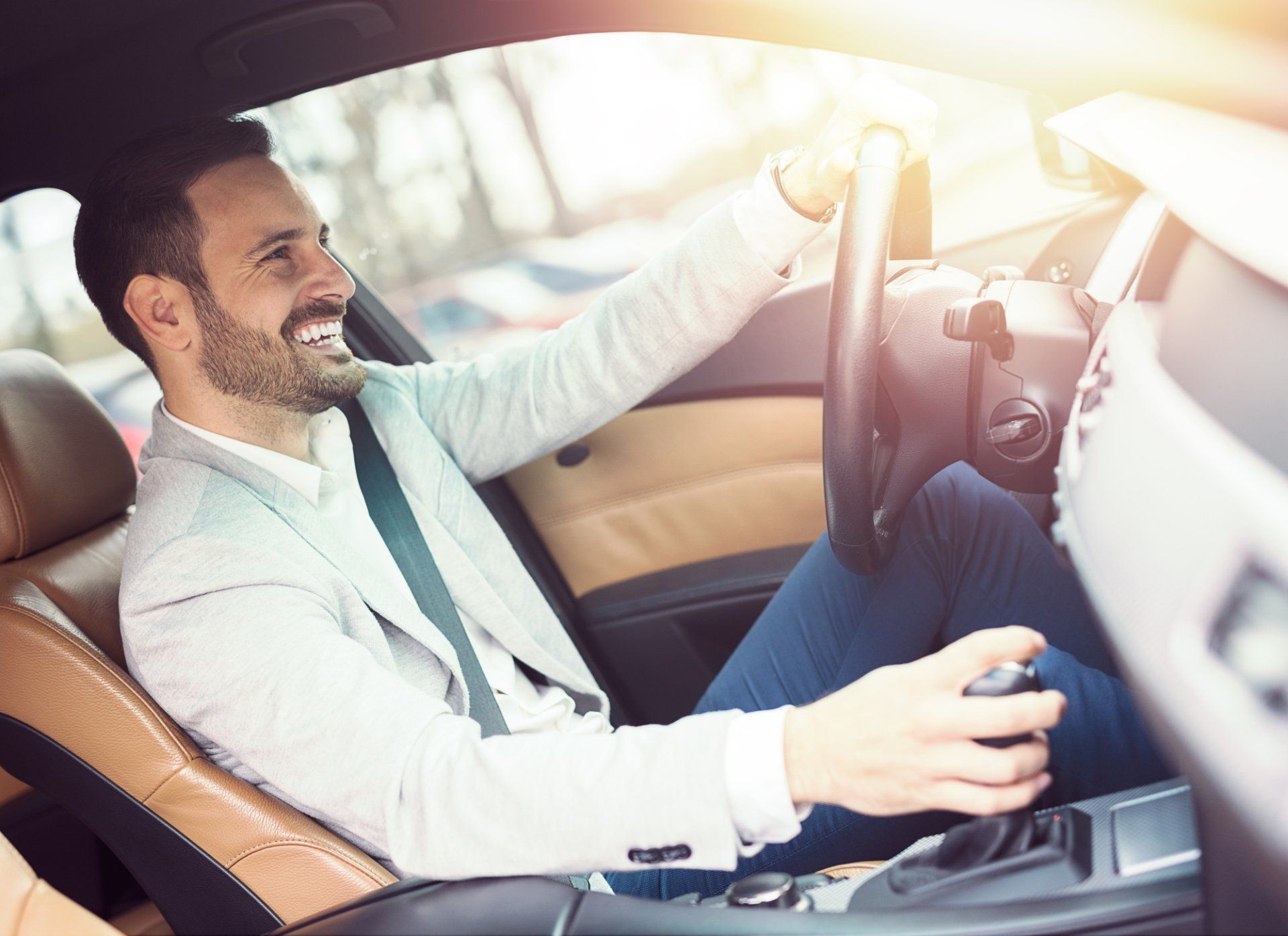 A man in a suit is driving a car and smiling.