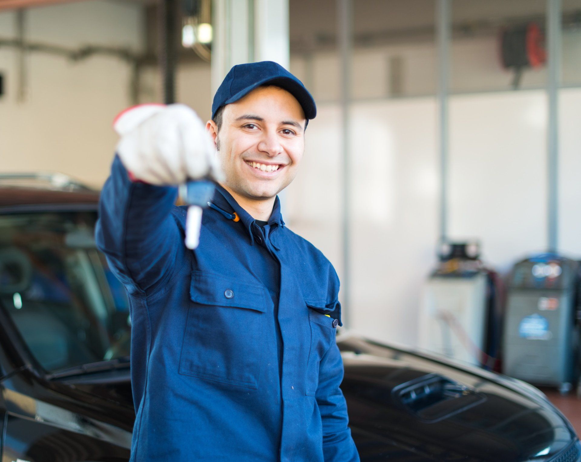 A mechanic is holding a car key in front of a car in a garage.