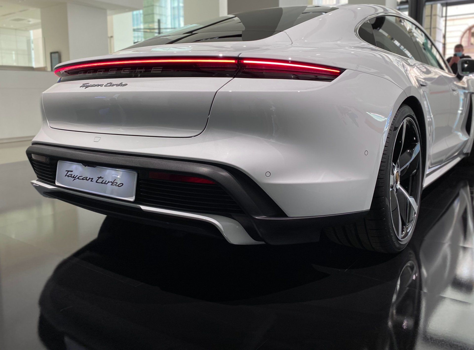 A white porsche taycan turbo is parked in a showroom.