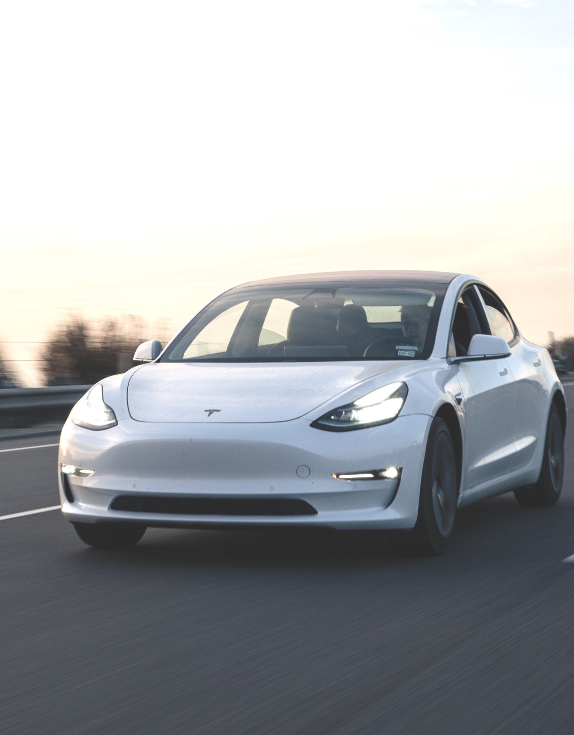 A white tesla model 3 is driving down a highway.