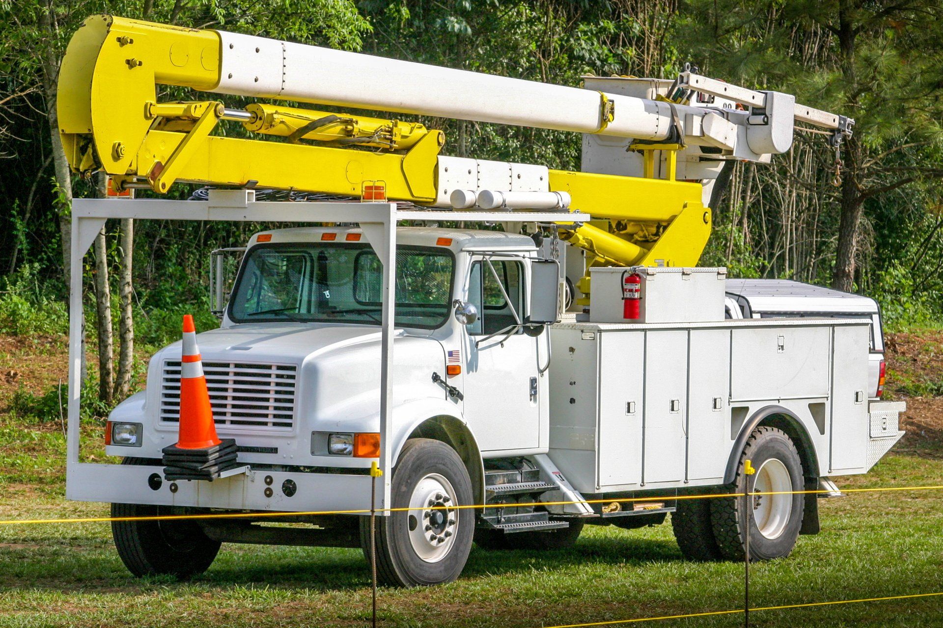A white truck with a yellow crane on top of it is parked in a grassy field.