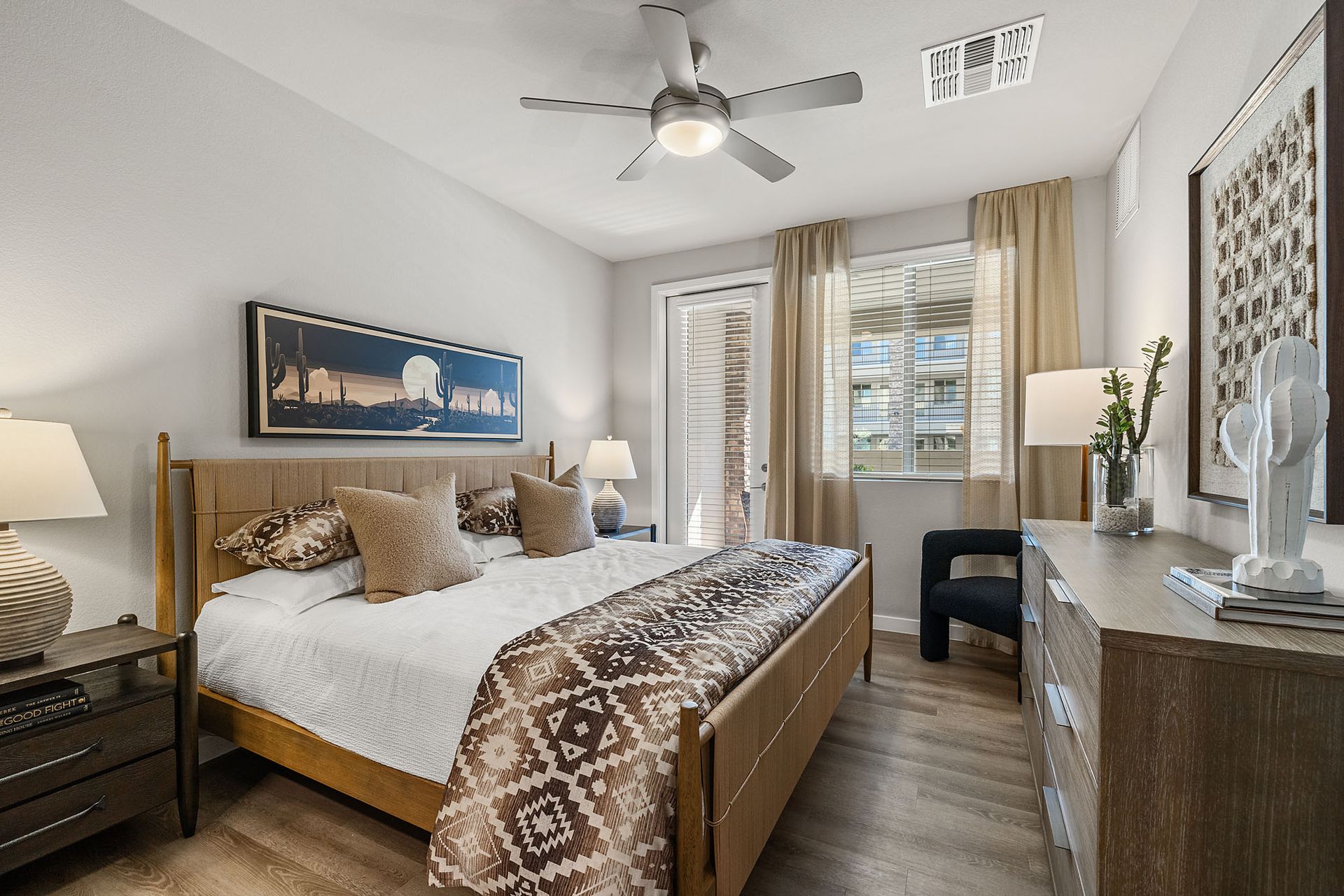 Bedroom with bed, nightstands, dresser, window, and ceiling fan. Warm tones, natural light at Marq Bronco Butte, offers 1, 2, and 3 bedroom apartments in North Phoenix, AZ.