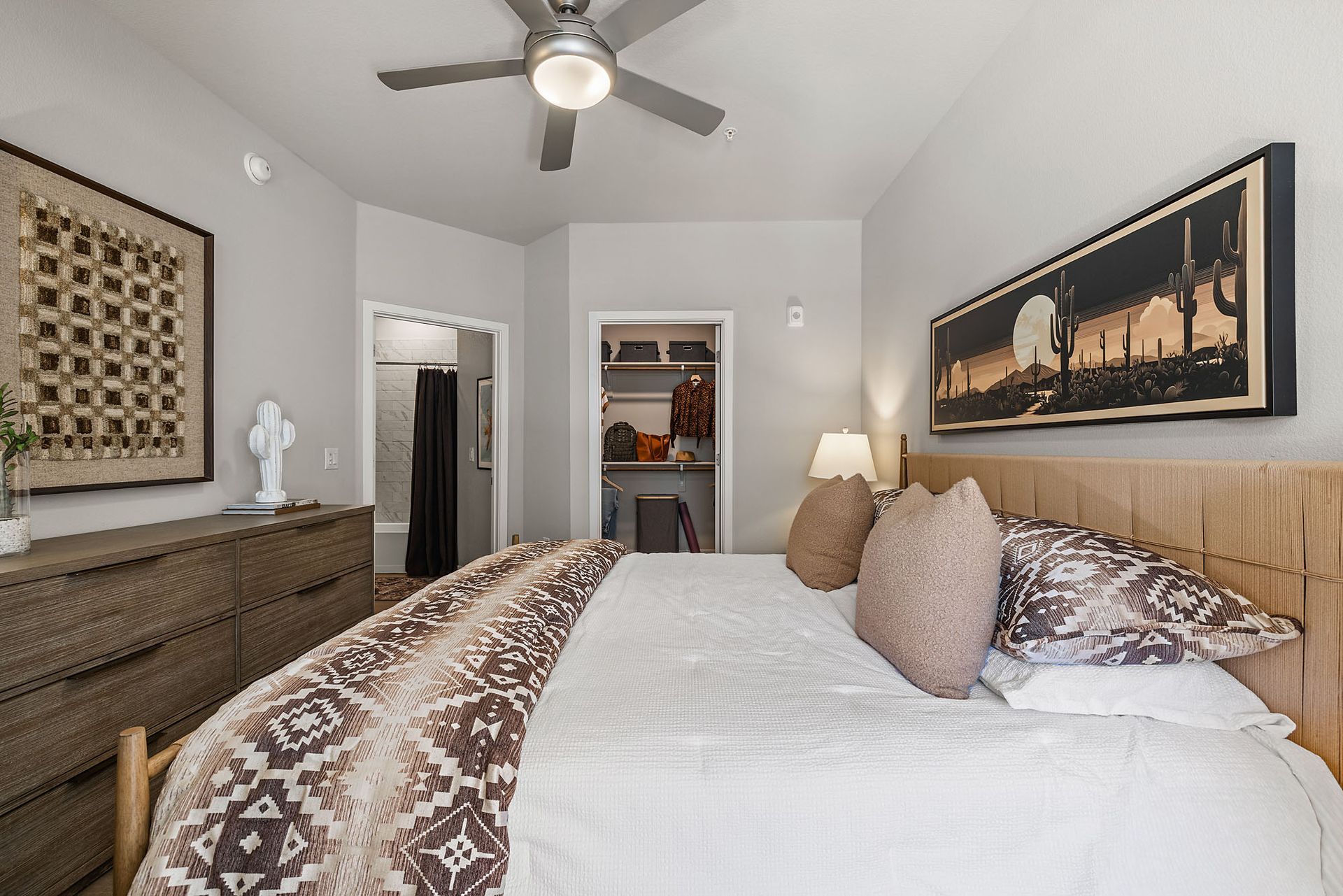 Bedroom with a king bed, dresser, art, and an open closet  at Marq Bronco Butte, offers  1, 2, and 3 bedroom apartments in North Phoenix, AZ. The room has neutral tones.