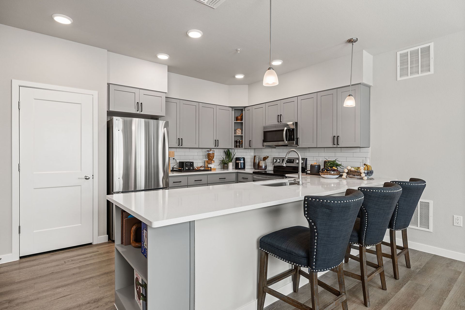 Modern kitchen with gray cabinets, white countertop island, and three blue bar stools at Marq Bronco Butte, offers apartments in North Phoenix, AZ.
