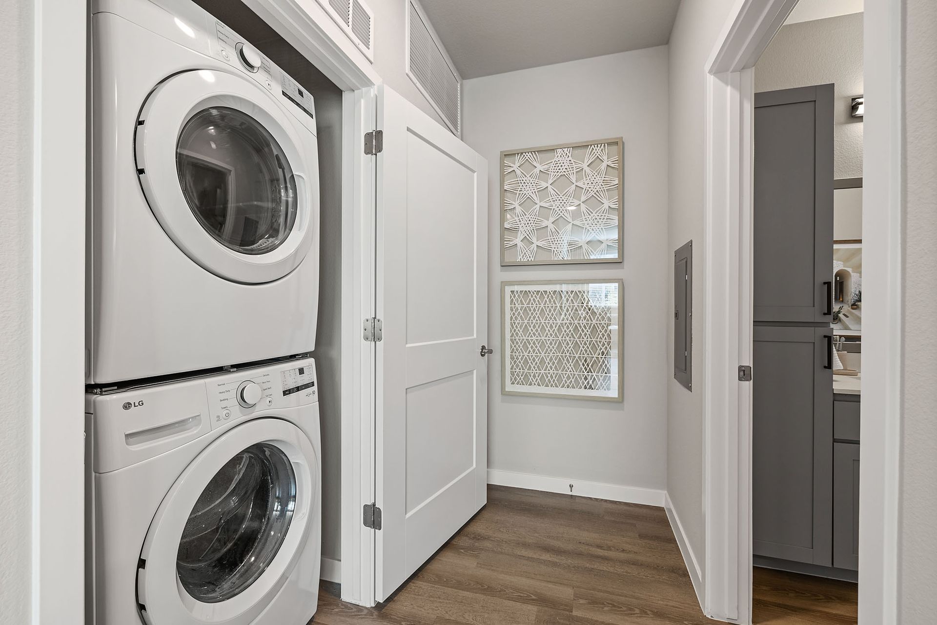 Stacked washer and dryer in a laundry room, next to a closed door and framed artwork at Marq Bronco Butte, offers 1, 2, and 3 bedroom apartments in North Phoenix, AZ.