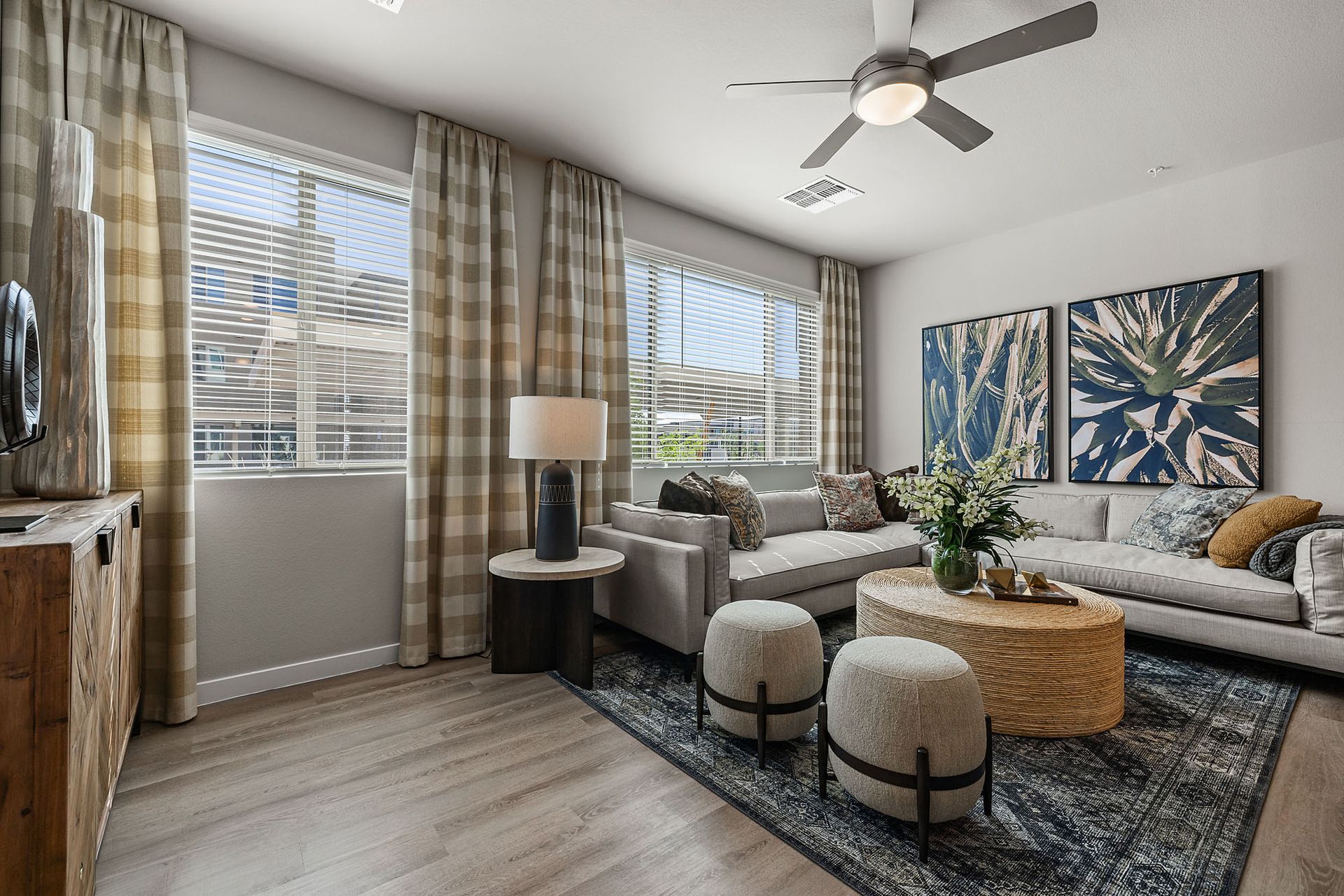 Living room with gray sofa, patterned rug, coffee table, two patterned stools, and windows with plaid curtains at Marq Bronco Butte, offers apartments in North Phoenix, AZ.
