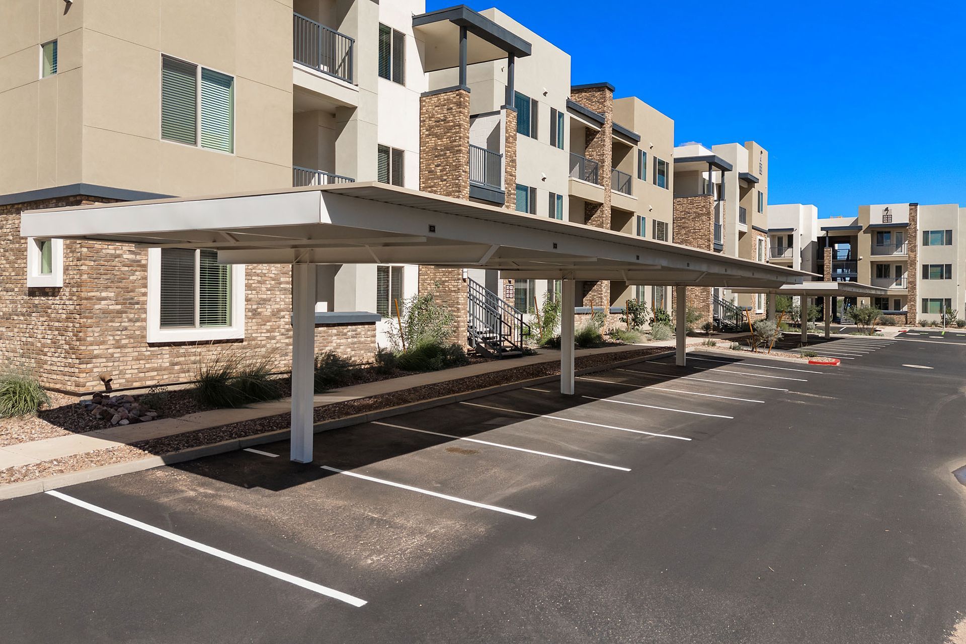 Carport shading parking spaces at a beige apartment building with stone accents at Marq Bronco Butte, offers 1, 2, and 3 bedroom apartments in North Phoenix, AZ.