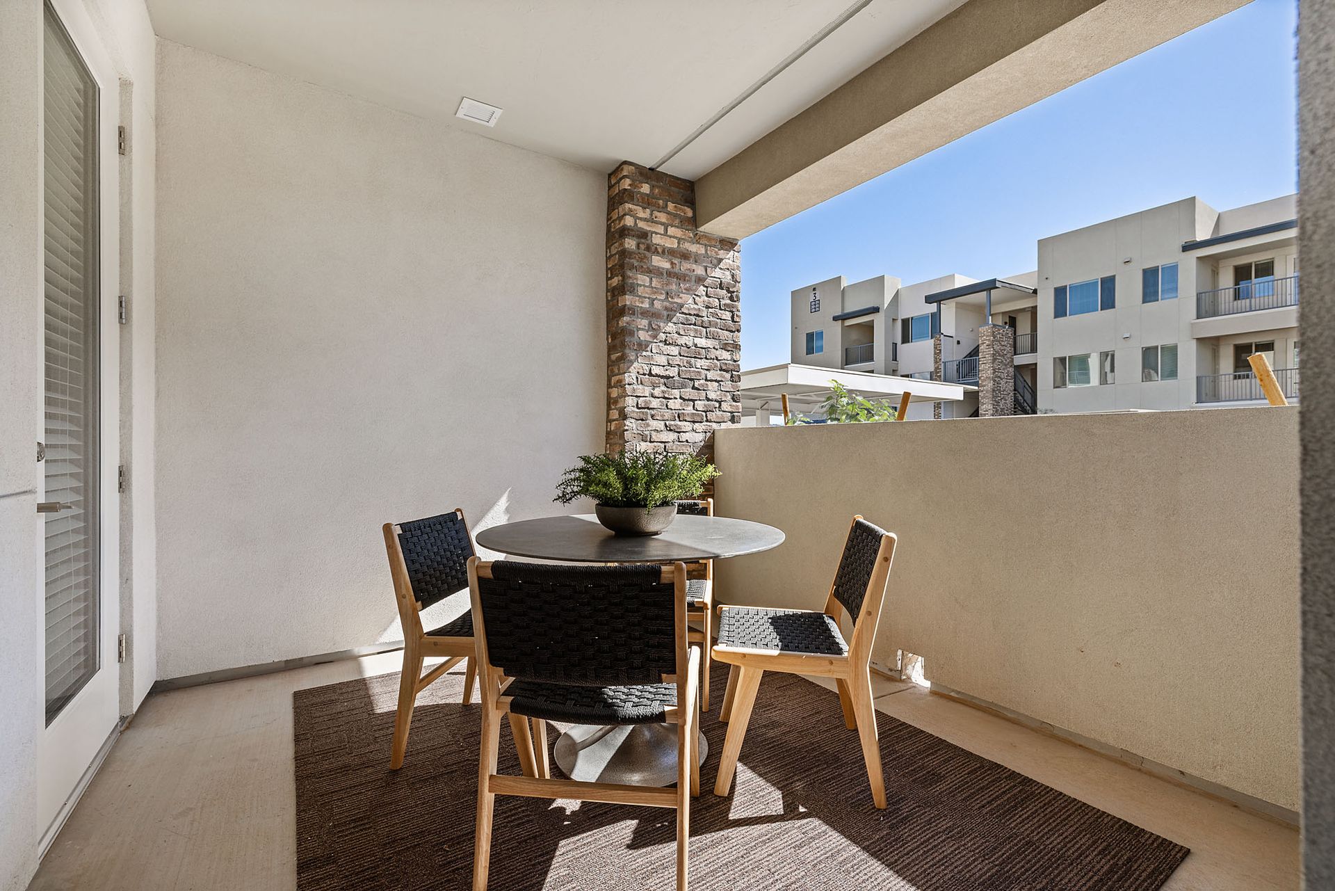 Balcony with table and chairs; view of other buildings at Marq Bronco Butte, offers 1, 2, and 3 bedroom apartments in North Phoenix, AZ, with smart home features. Sunny day, neutral color tones.