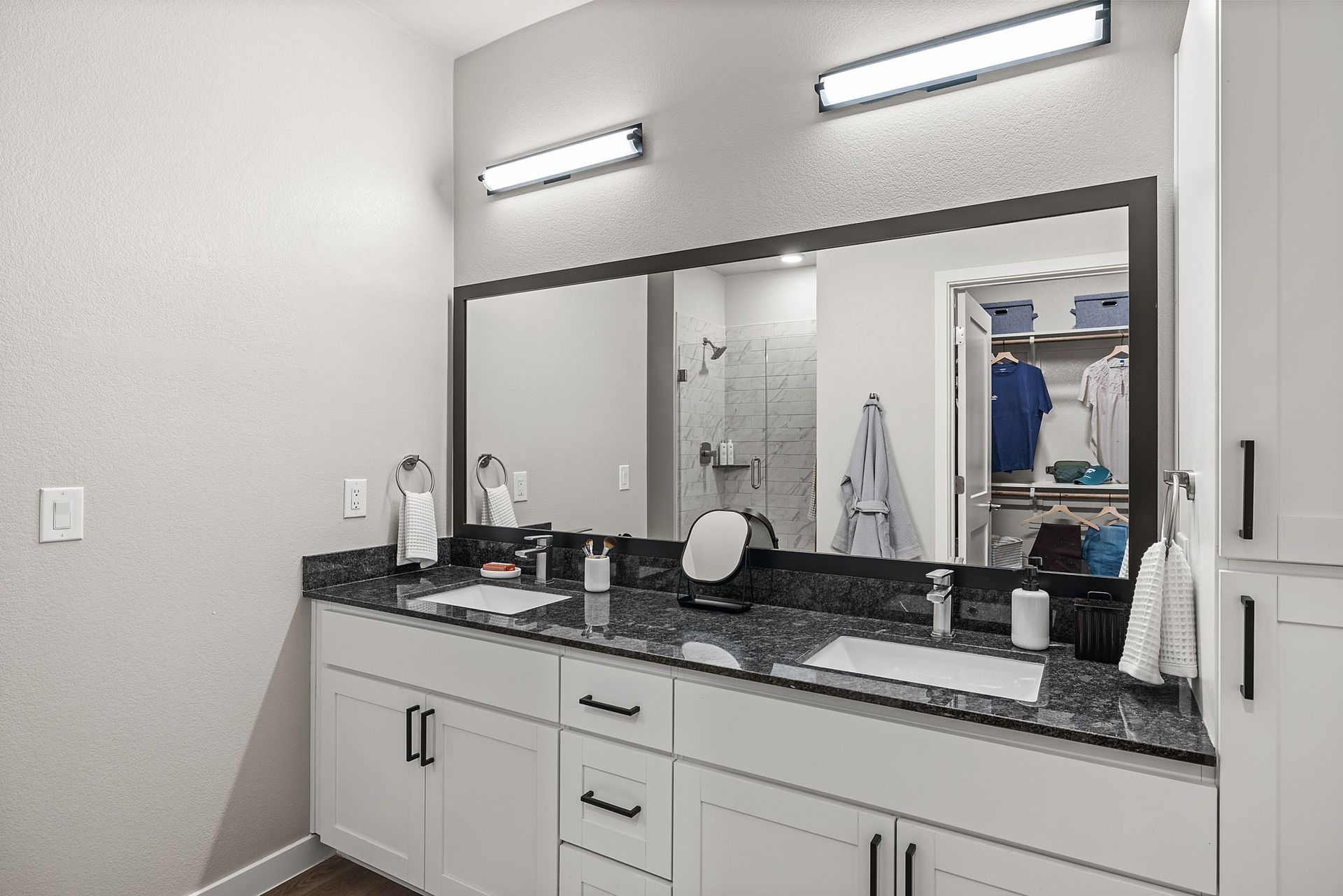 Bathroom with double sinks, large mirror, white cabinets, dark countertop, and closet at Marq Bronco Butte, offers loft-style apartments in North Phoenix, AZ.