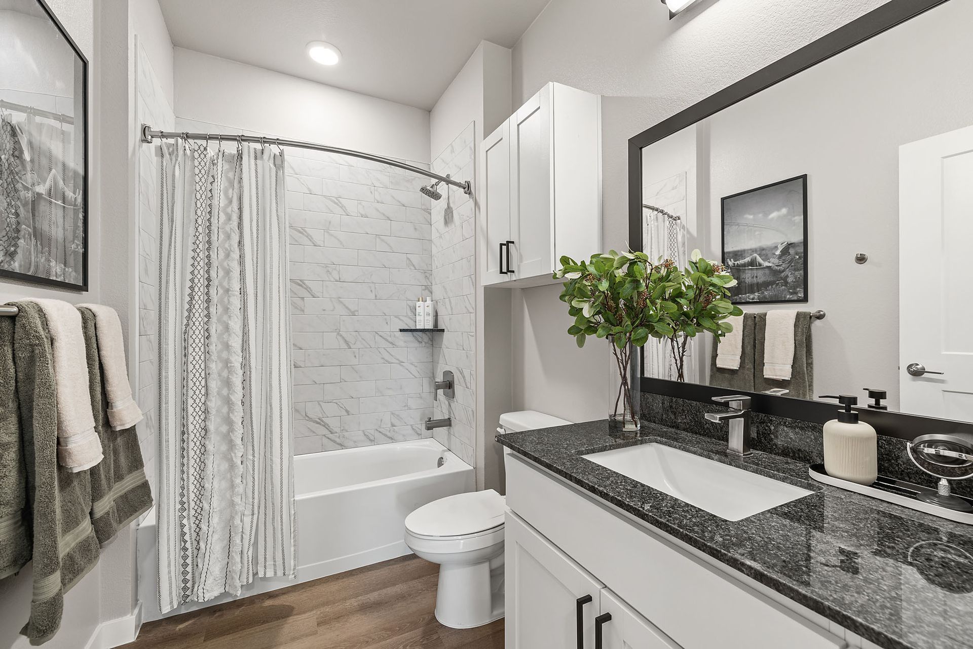 Bathroom with white walls, tub, and toilet. Black countertop, large mirror, and decorative items at Marq Bronco Butte, offers loft-style apartments in North Phoenix, AZ.