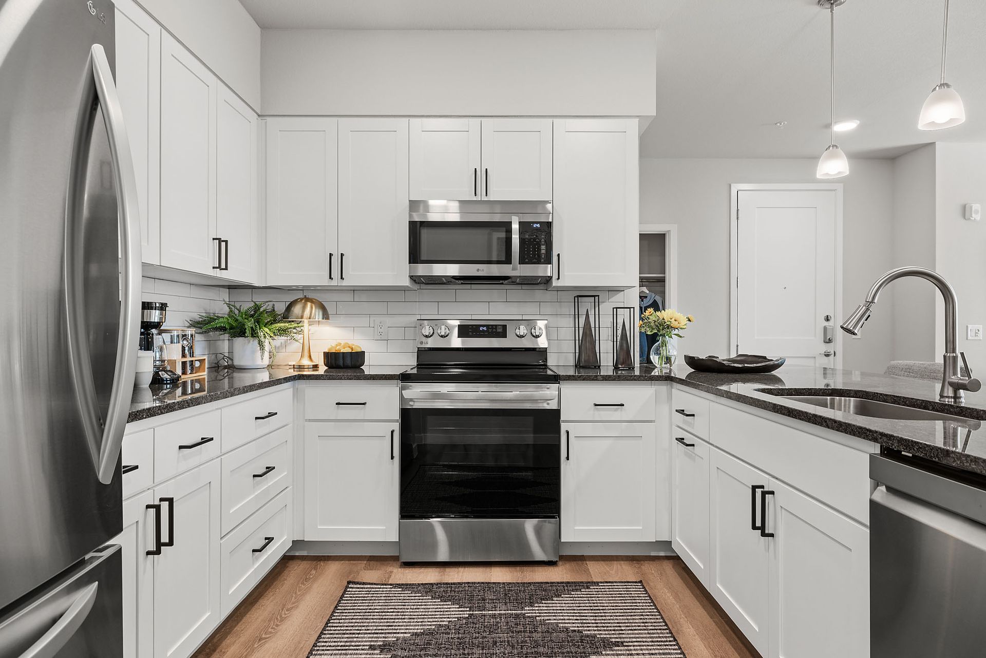 Modern white kitchen with stainless steel appliances, black countertops, and wooden floors at Marq Bronco Butte, offers pet-friendly apartments in North Phoenix, AZ.