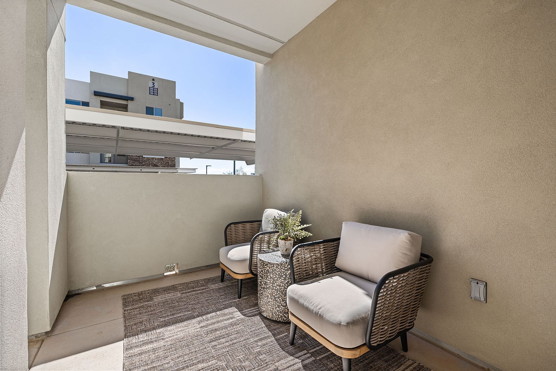 Small balcony with two chairs, a small table, rug, and plants at Marq Bronco Butte, offers apartments in North Phoenix, AZ. Light beige walls and blue sky.