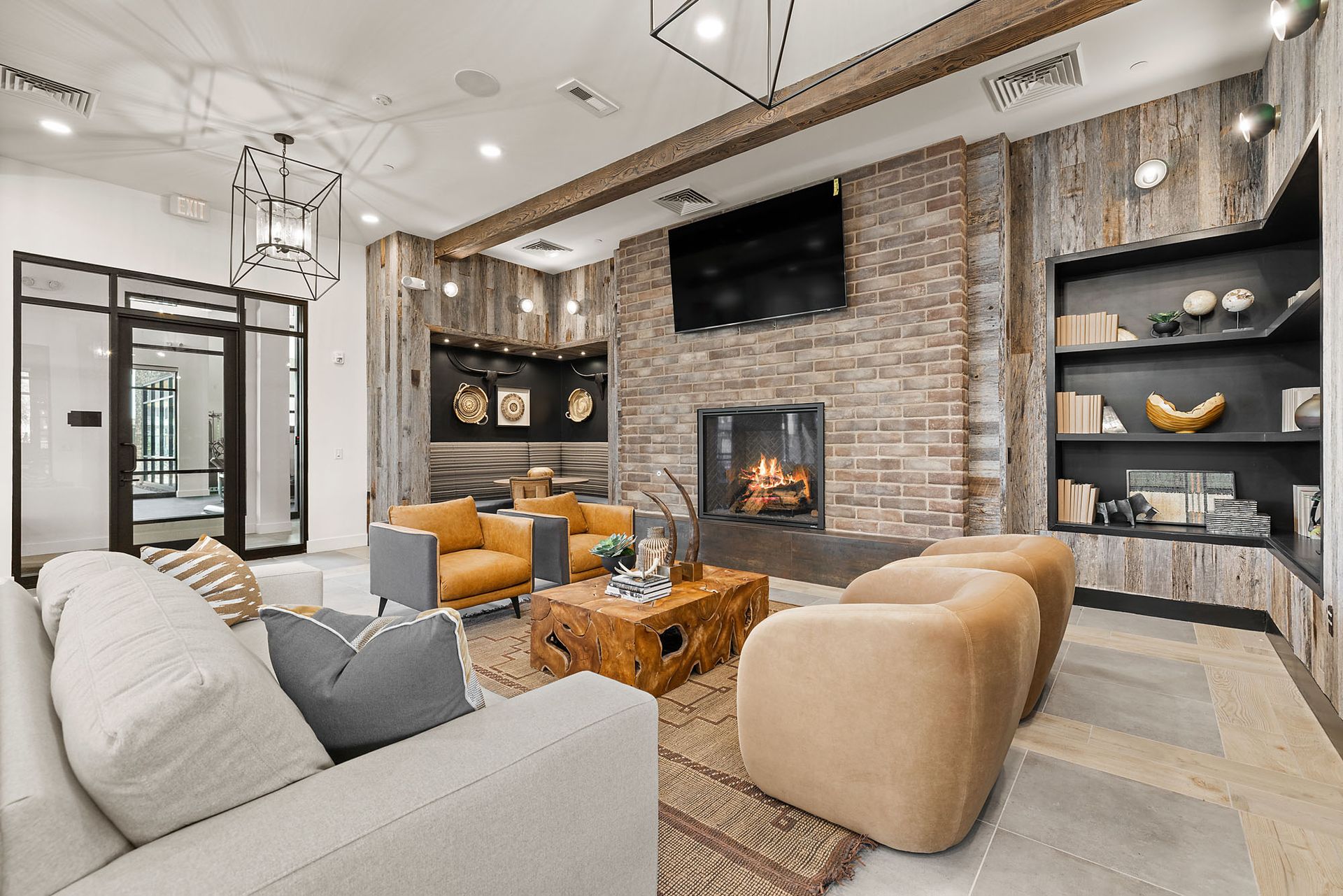 Lounge area with fireplace, seating, bookshelf, and TV at Marq Bronco Butte, offers brand-new apartments in North Phoenix, AZ. Wooden beams and accent wall add texture.