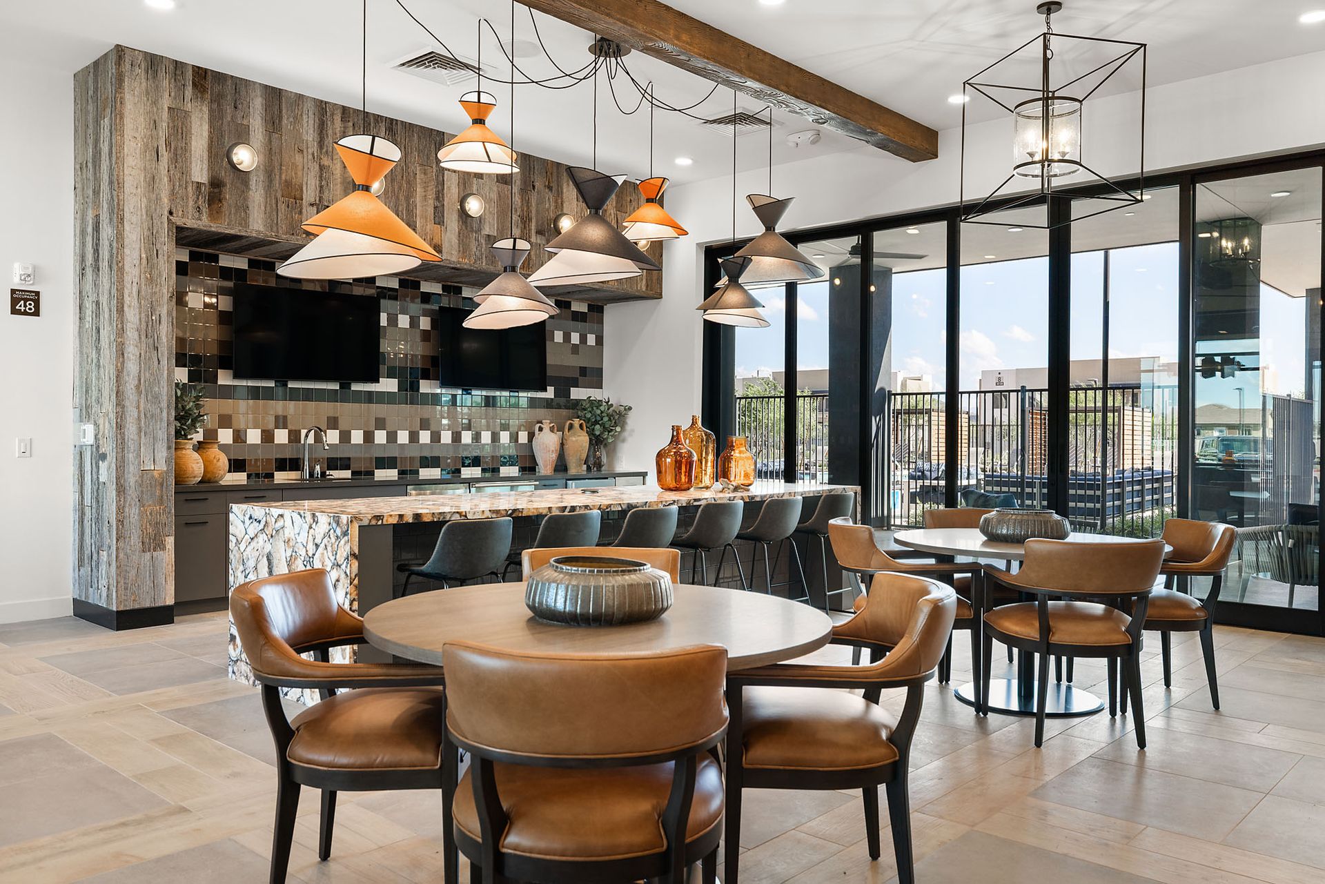 Lounge area with bar, tables, and leather chairs at Marq Bronco Butte, offers brand-new apartments in North Phoenix, AZ. Rustic wood accents, hanging lights, and large windows.
