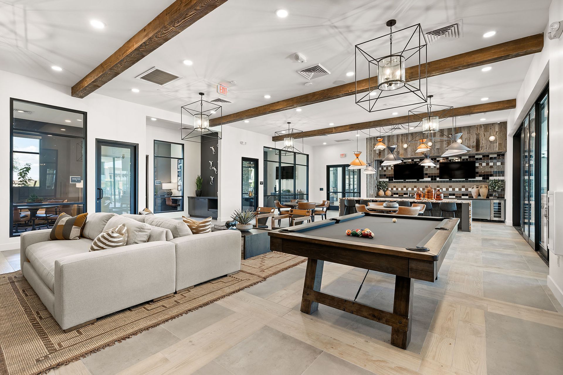 Spacious lounge with pool table, bar area, and large windows at Marq Bronco Butte, offers brand-new apartments in North Phoenix, AZ. White walls, exposed wooden beams, and neutral-toned furniture.