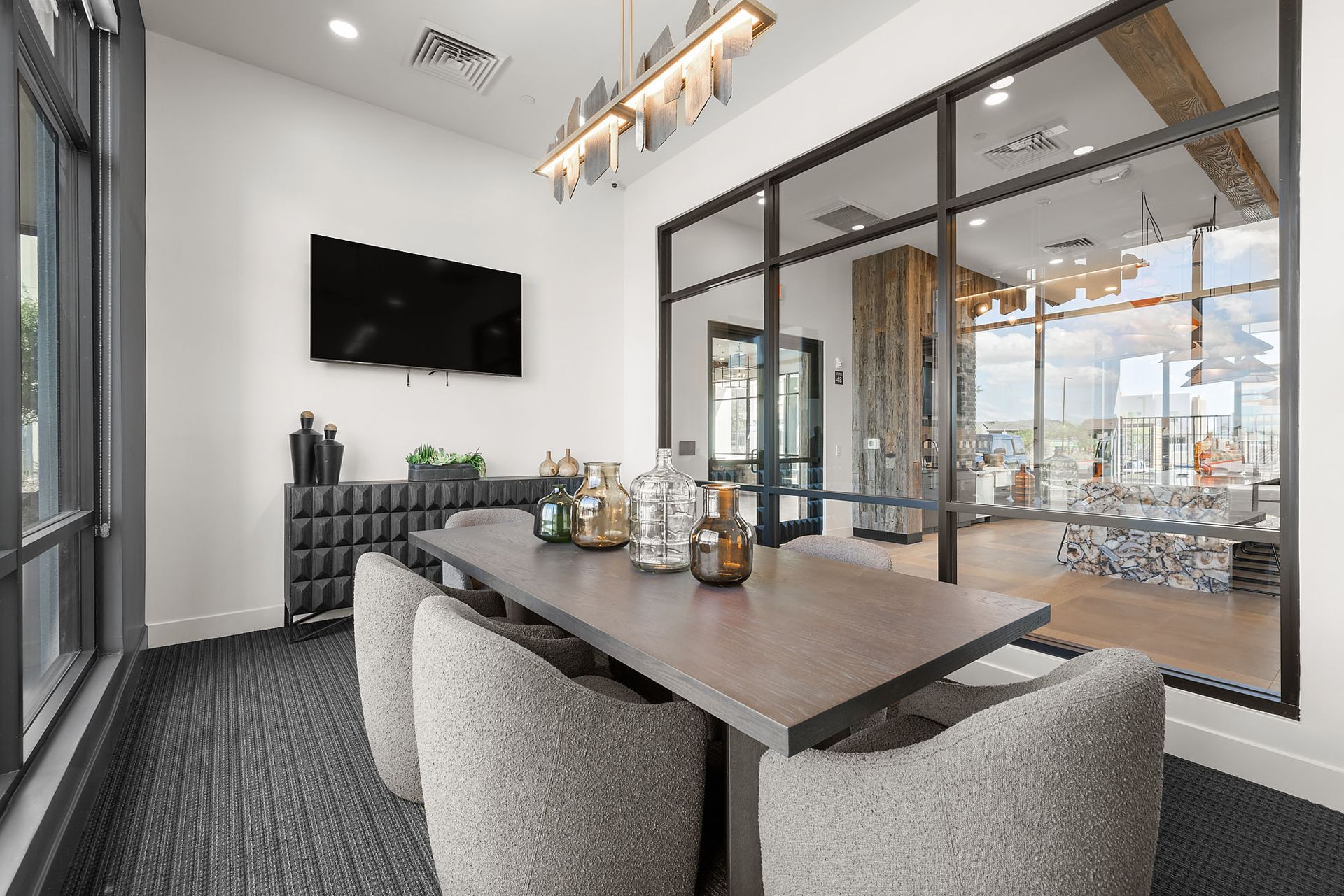 Meeting room with a long table, chairs, TV, and decorative items at Marq Bronco Butte, offers brand-new apartments near TSMC in North Phoenix, AZ. Large glass wall to a common area.