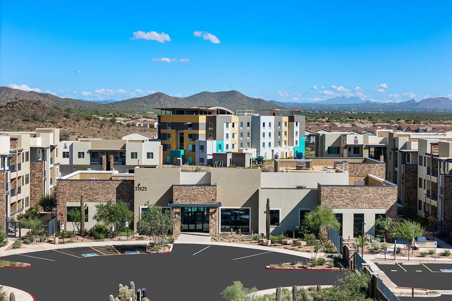 Modern apartment complex with multi-colored buildings, surrounded by desert landscape and mountains at Marq Bronco Butte, offers brand-new apartments for rent in North Phoenix, AZ.