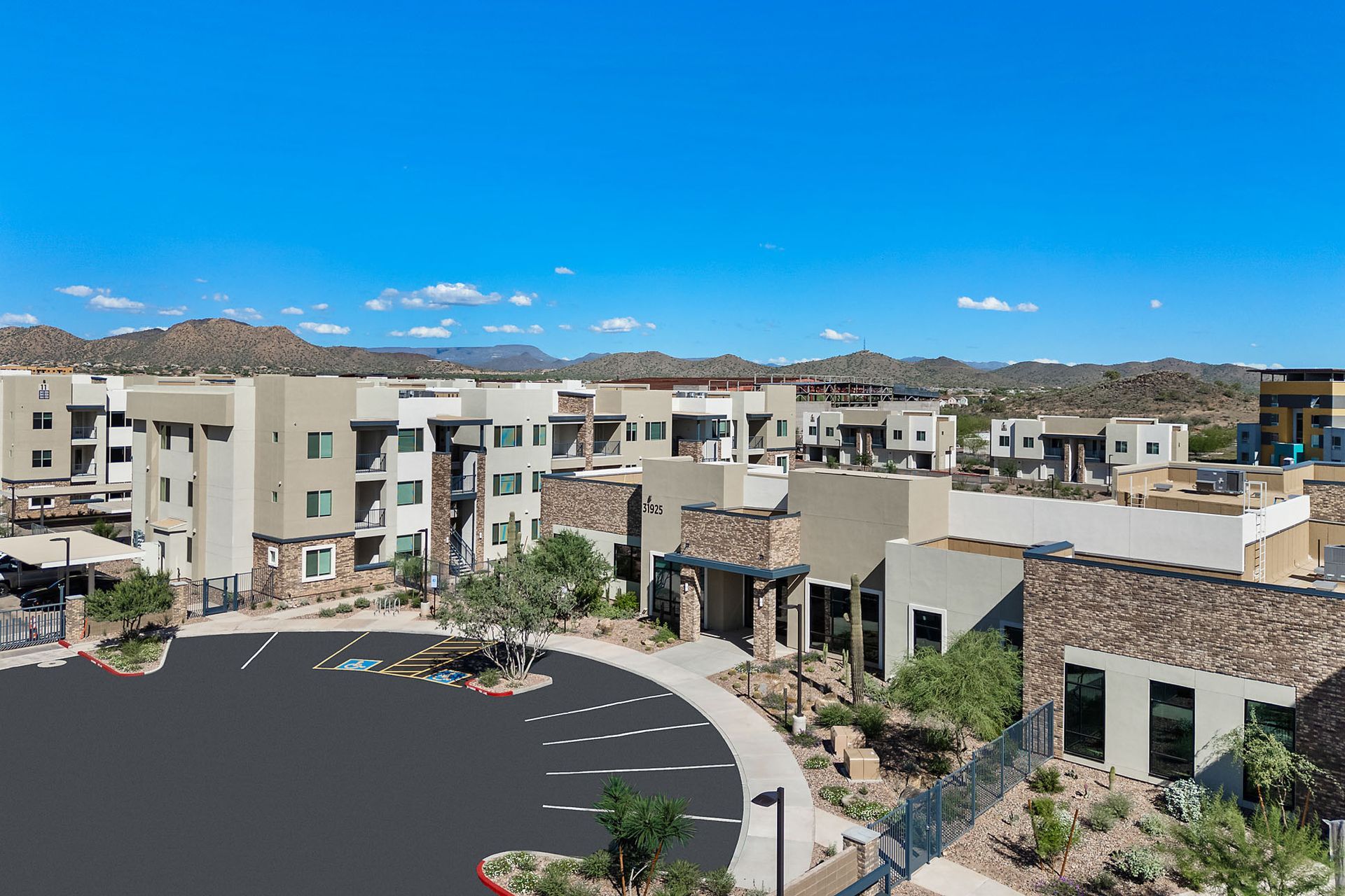 Apartment complex with beige buildings, surrounded by desert landscaping and mountains under a blue sky at Marq Bronco Butte, offers brand-new apartments for rent in North Phoenix, AZ.
