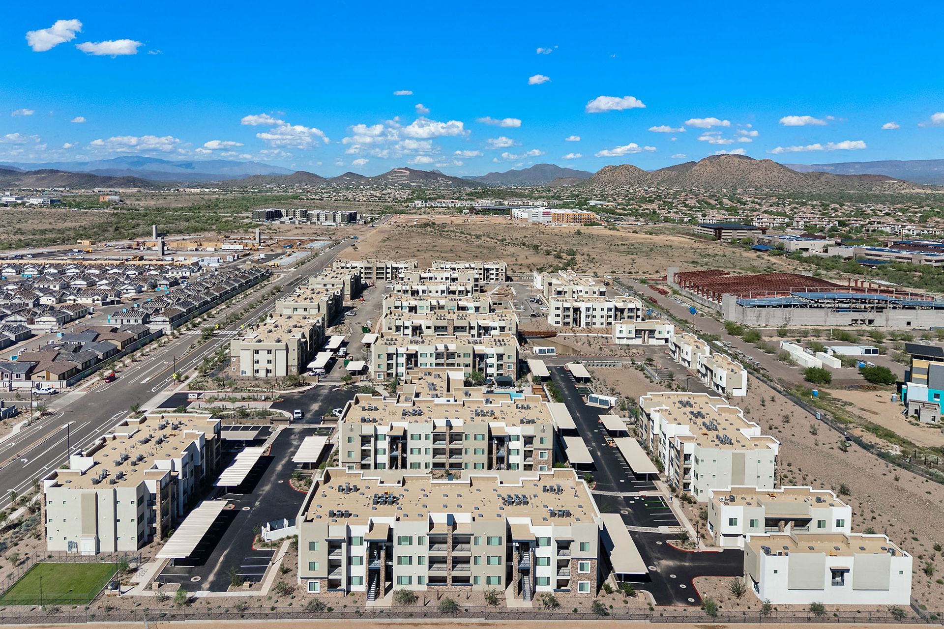Aerial view of apartment buildings in a desert landscape under a blue sky with mountains in the background at Marq Bronco Butte, offers 1, 2, and 3 bedroom apartments in North Phoenix, AZ.