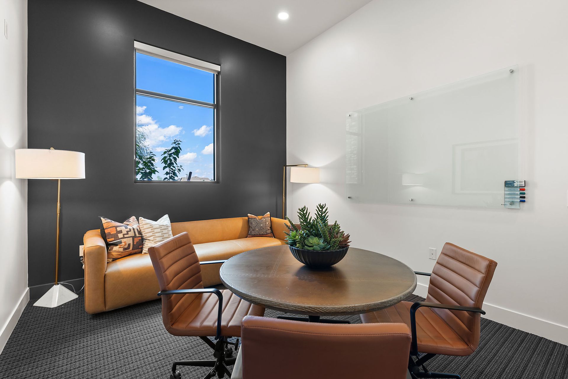 Conference room with leather chairs around a wooden table, sofa, window, and whiteboard at Marq Bronco Butte, offers brand-new apartments near TSMC in North Phoenix, AZ.
