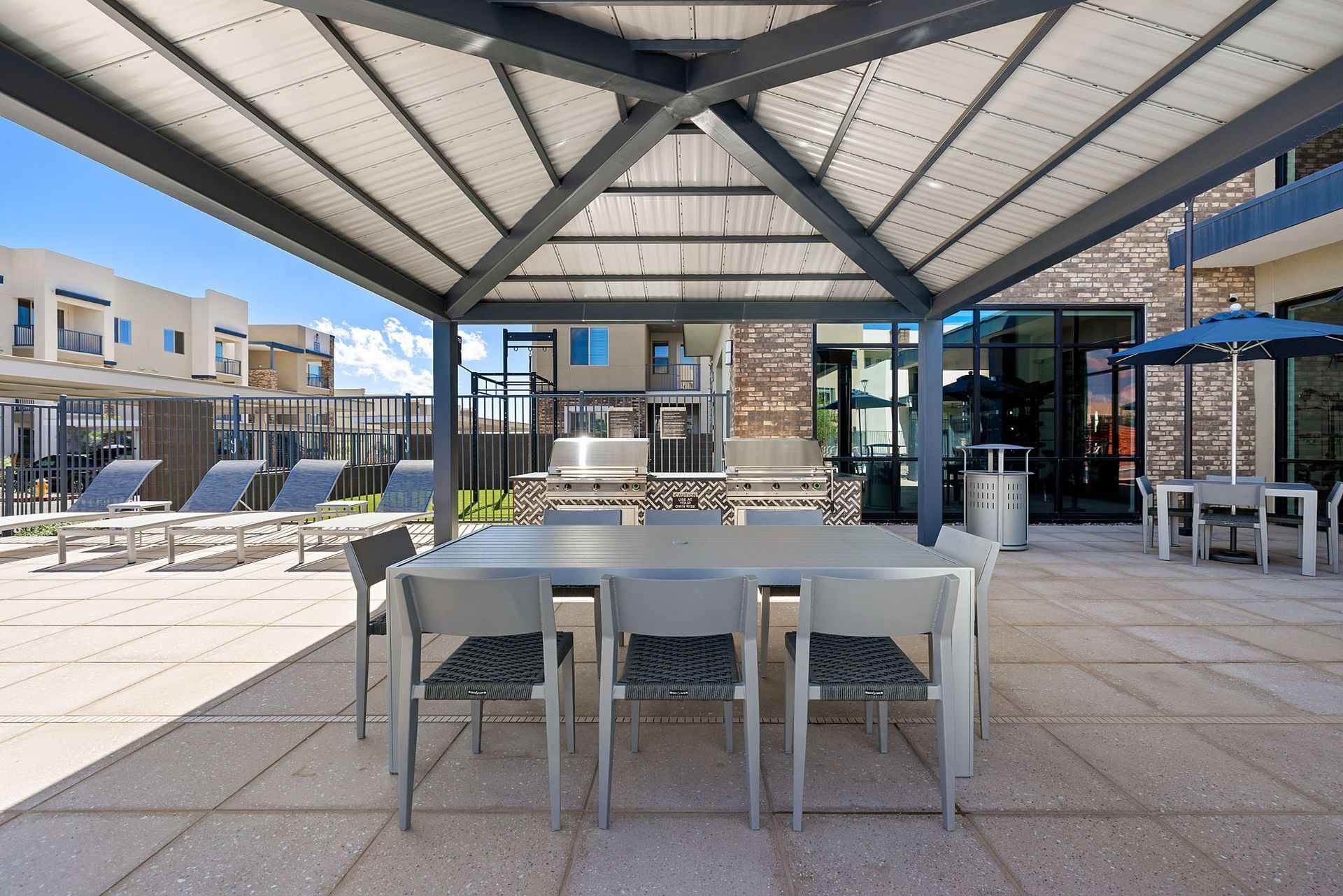 Patio with table, chairs, and shade structure; lounge chairs and building in background at Marq Bronco Butte, offers apartments near Dove Valley Towne Center in North Phoenix, AZ.