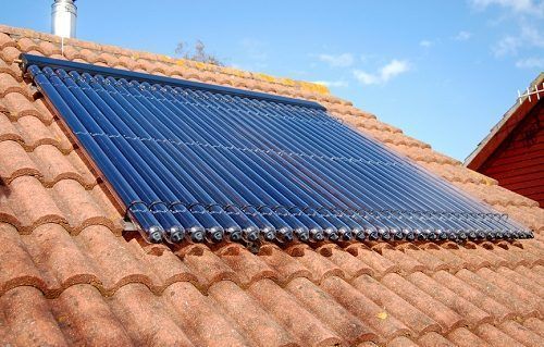 Pannelli solari blu per il riscaldamento dell'acqua su un tetto di tegole di terracotta sotto un cielo limpido