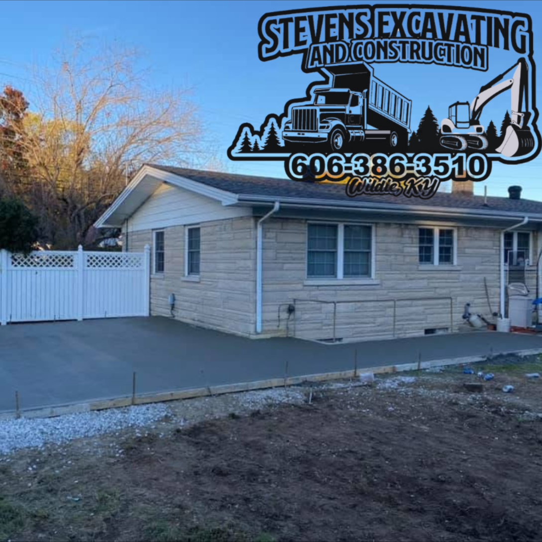 New concrete driveway next to a beige house. Stevens Excavating logo in the corner with phone number.