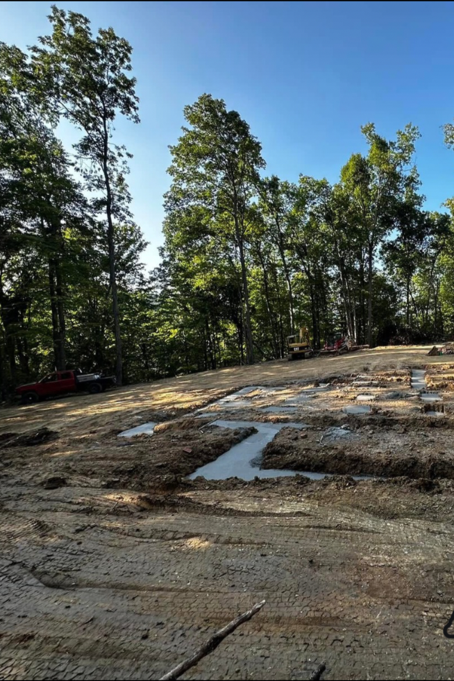 Construction site with tree line; foundation outlines marked in wet cement, ground is dirt.
