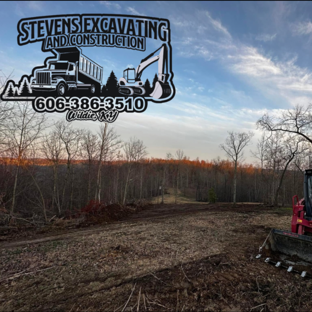 Stevens Excavating site clearing with excavator, truck logo, phone number. Blue sky, woods.