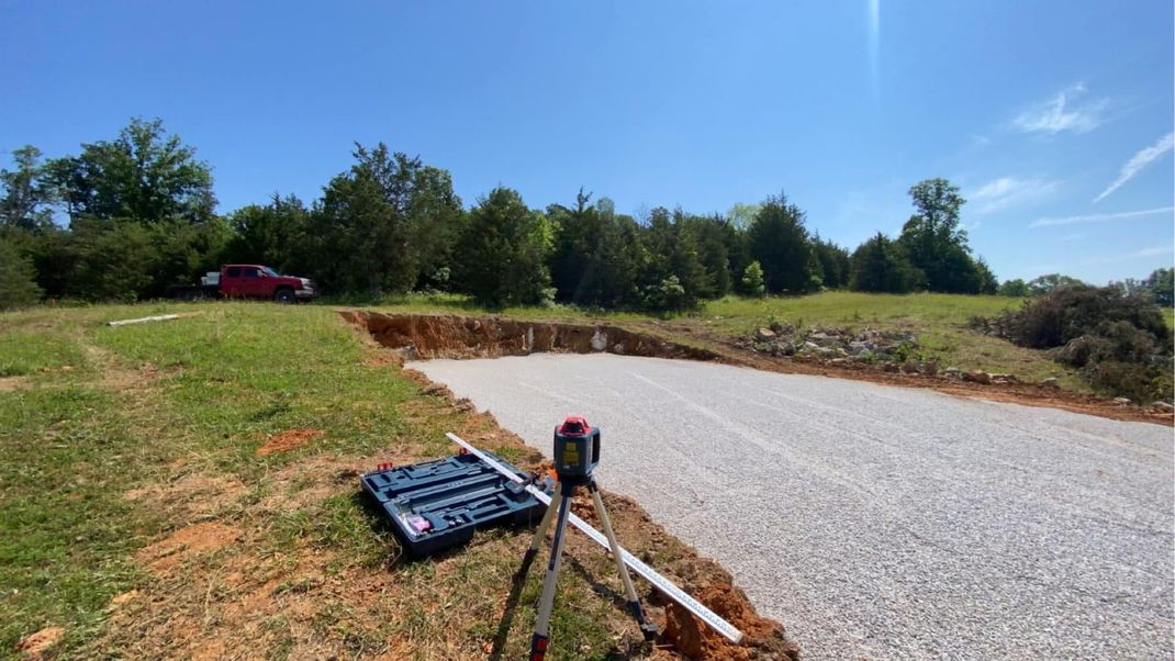 Gravel driveway under construction with a laser level on a tripod, on a sunny day.