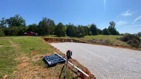 Gravel driveway under construction with a laser level on a tripod, on a sunny day.