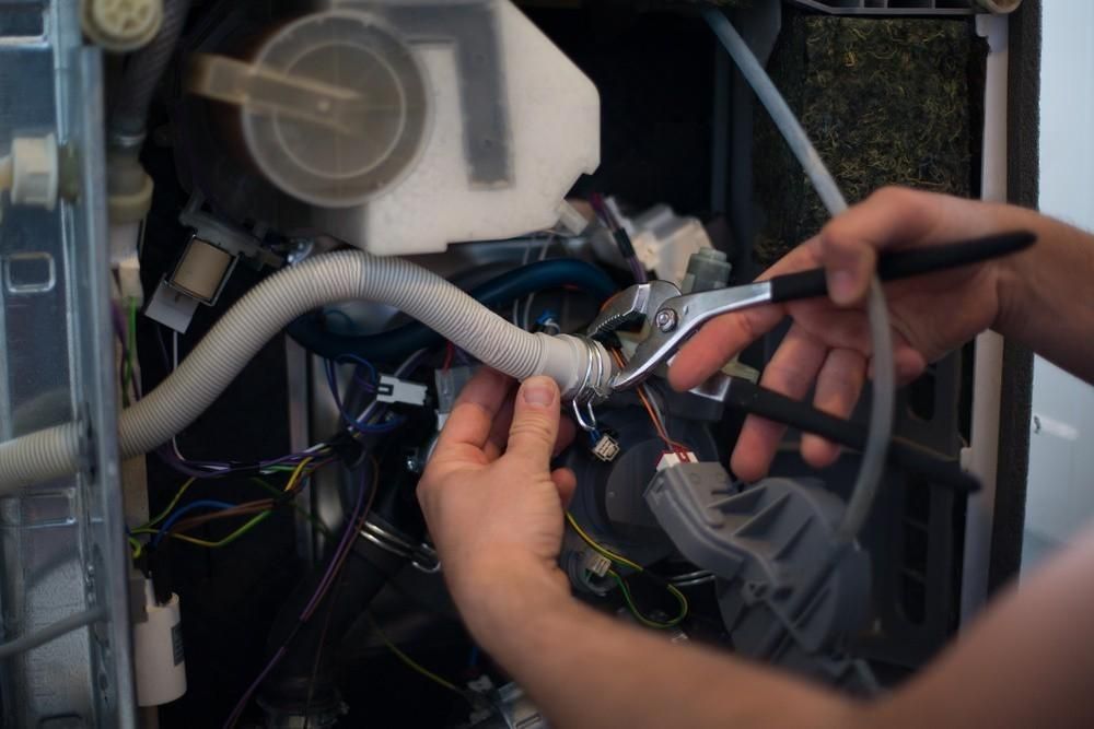 A person is fixing a dishwasher with pliers.