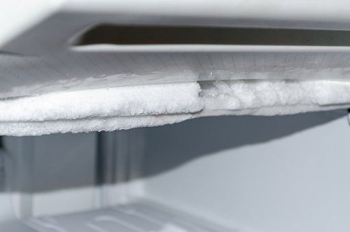 Close-up of a freezer compartment with a significant build-up of ice covering the interior surfaces and shelves.