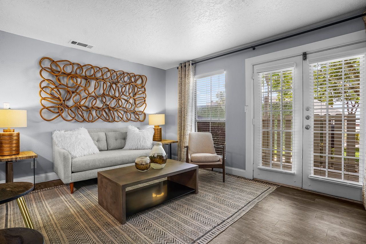 Living room at Telegraph Hill with a gray sofa, wood coffee table, wall sculpture, and glass doors with blinds.