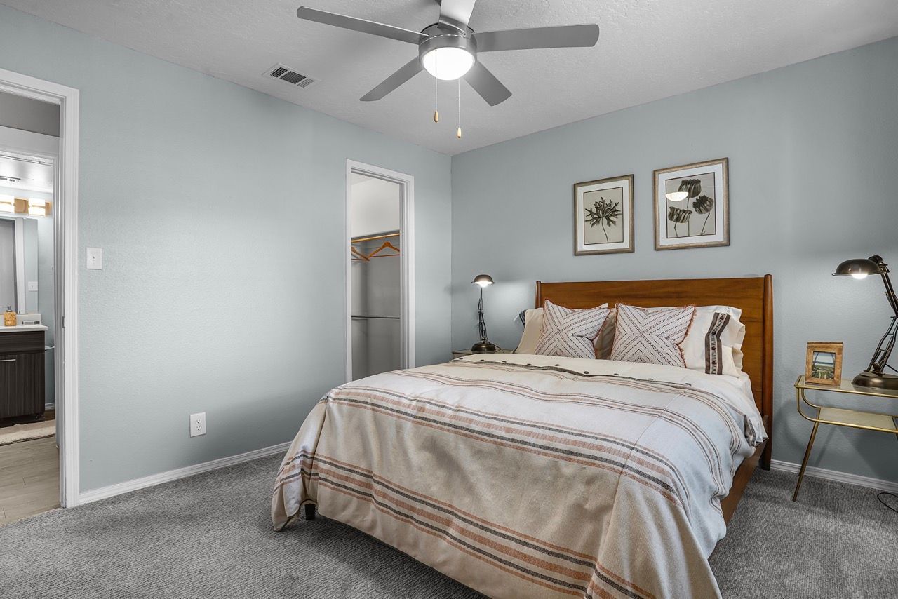 Bedroom in an apartment with a queen bed, two nightstands, lamps, and a ceiling fan.