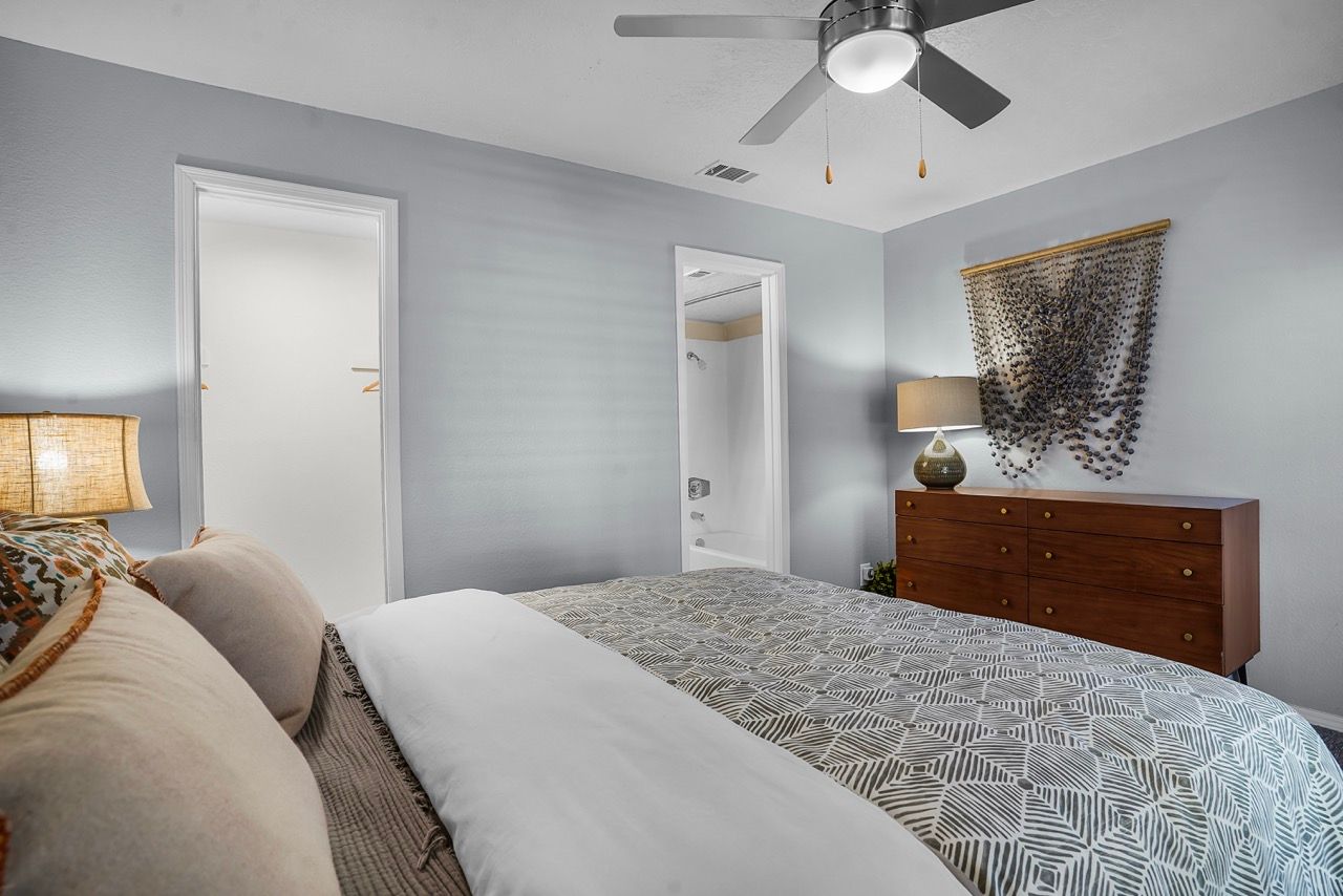 Bedroom in apartment with large bed, dresser, lamp, and ceiling fan.