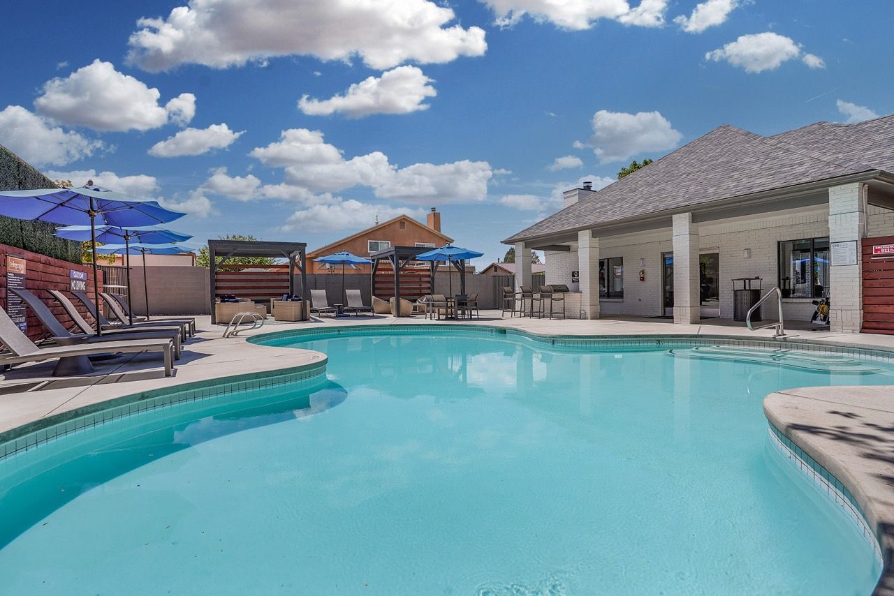 Telegraph Hill apartment pool area with lounge chairs, blue umbrellas, and a clubhouse nearby.